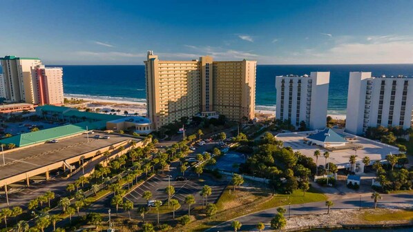 A coastal hotel complex with multiple high-rise buildings, a parking area, and a beach view. - Pelican Beach 1911 1 Bedroom Condo (Destin)