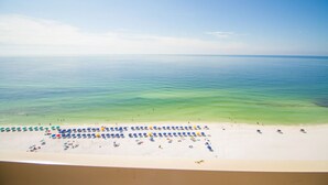 En strand med krystalklart turkis vand, hvidt sand og mange farverige parasoller.
