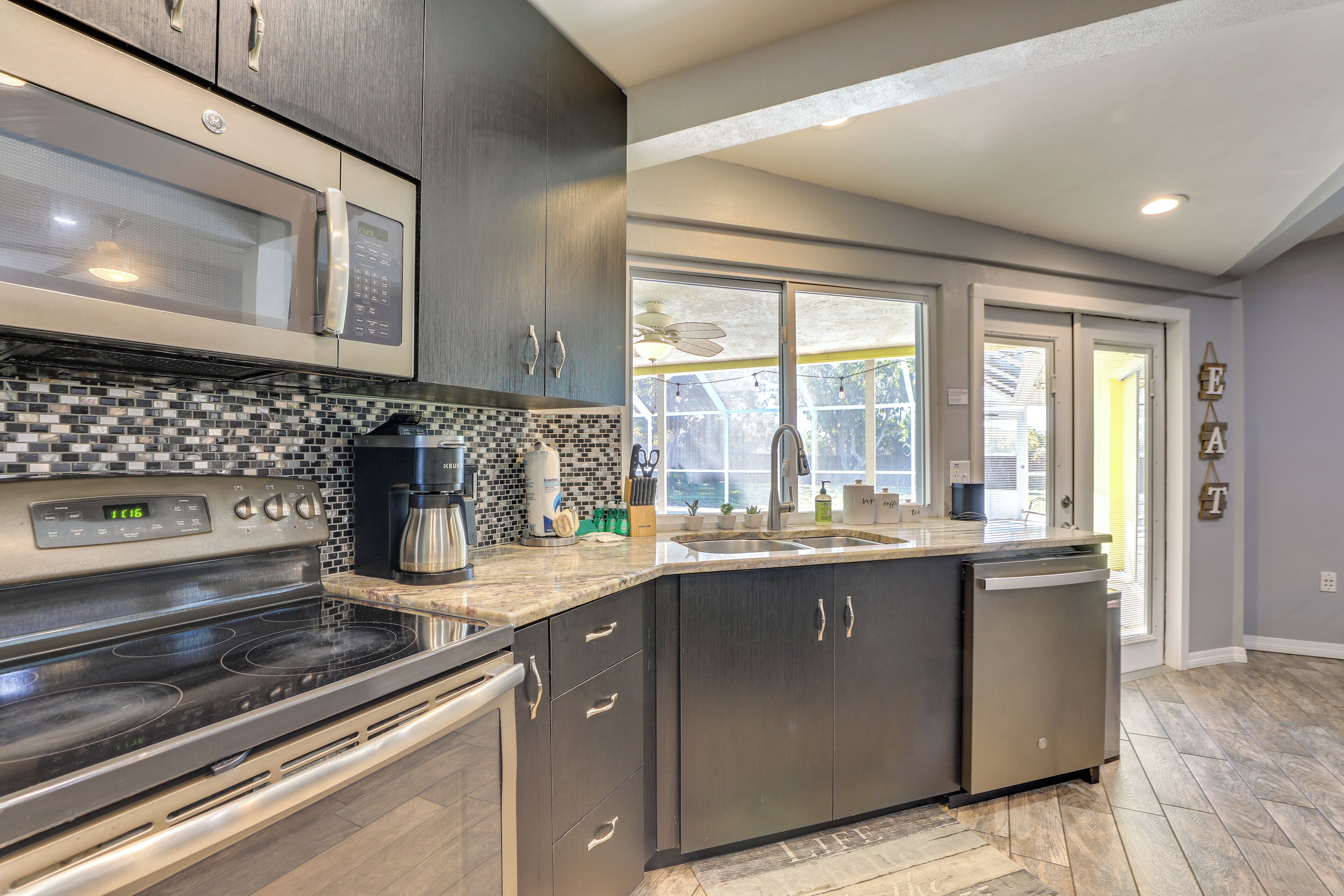 A modern kitchen with dark cabinetry, a stainless steel stove, and a large window providing natural light.