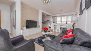 A modern living room with a grey sofa, a flat-screen TV, and a dining area with white chairs. - Villa Ivan (Novigrad)