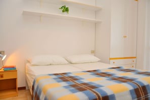 A bedroom with a bed, bedside table, lamp, and a shelf with a plant. - Relaxing Seaside Flat in a Modern Residence (San Michele al Tagliamento)