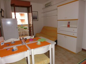 A small room with a bed, a table with a chair, a white wardrobe, and a window with a view of the outside. - Relaxing Seaside Flat in a Modern Residence (San Michele al Tagliamento)