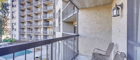 Un balcon avec des garde-corps en métal, un sol en béton et une piscine en arrière-plan.