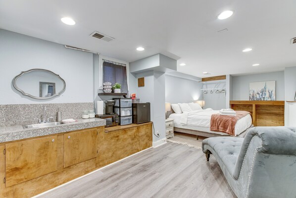 A modern bedroom with a large bed, bedside tables, and a grey upholstered chair. - 1 Mi to Coors Field: Cozy Denver Studio w/ Patio! (Denver)