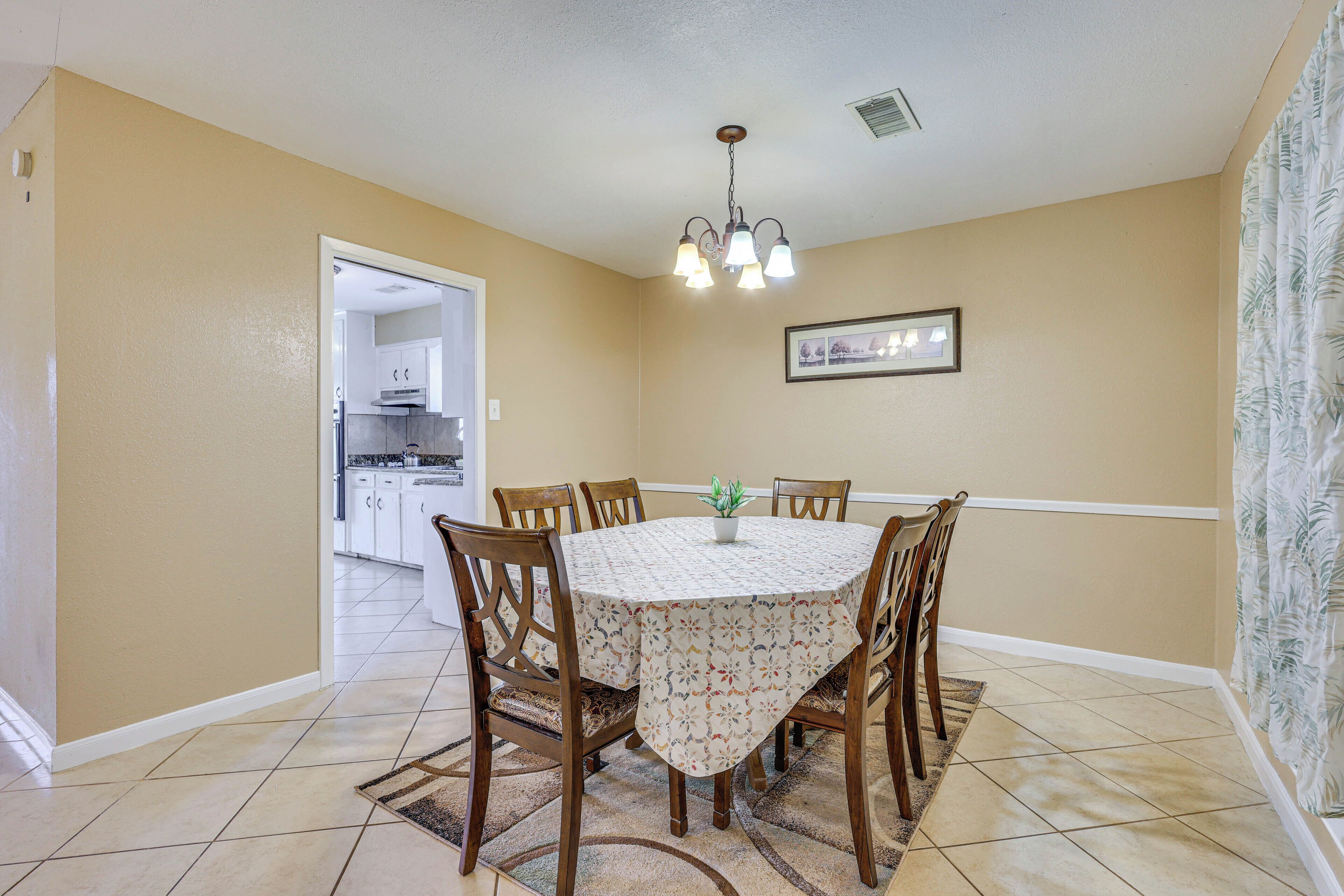 A dining room with a round table, six chairs, a chandelier, and a potted plant.