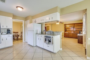 Una cocina con armarios blancos, un refrigerador, un horno y una zona de comedor con una mesa y sillas.