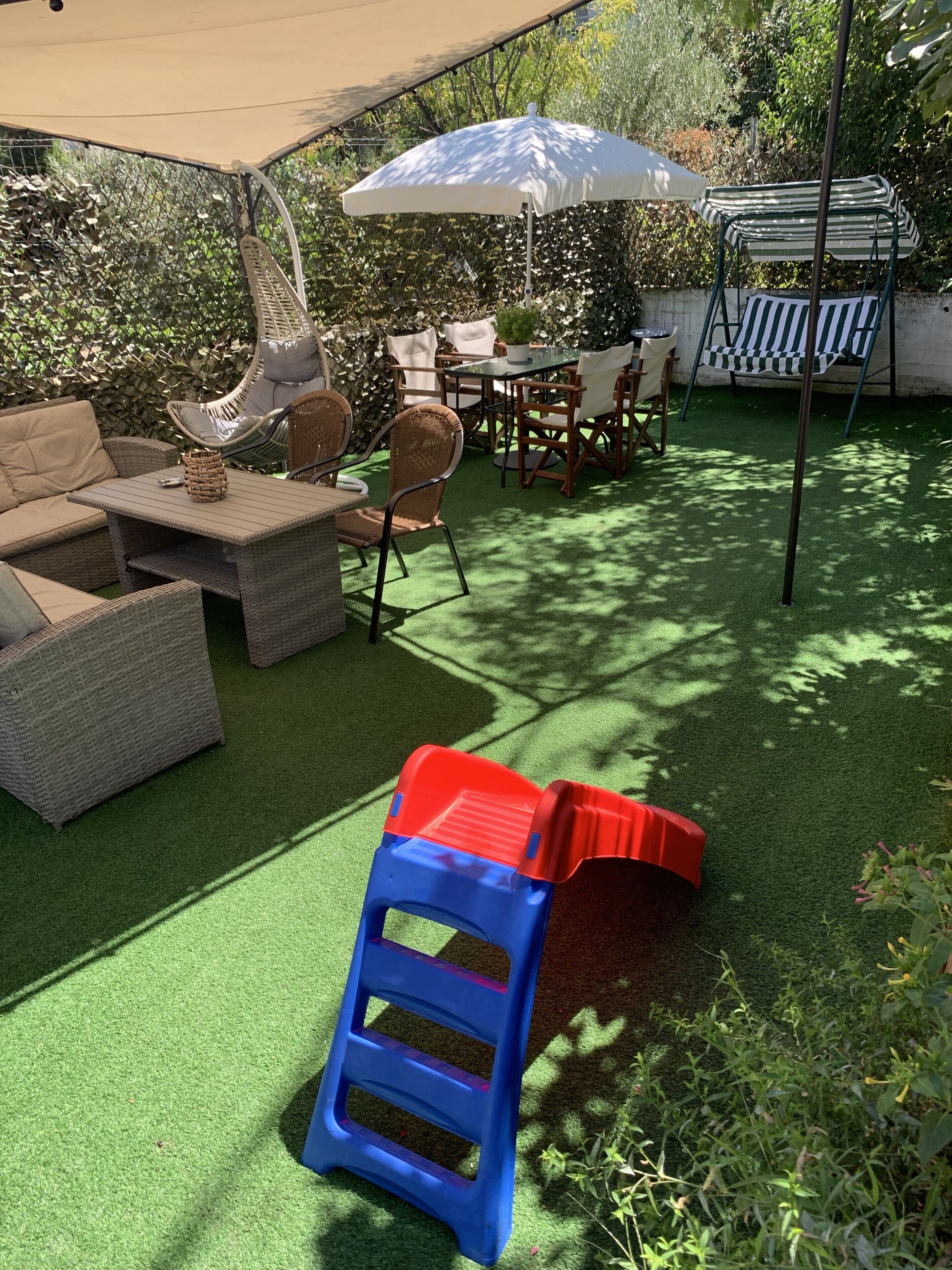 A patio area with outdoor furniture, a white umbrella, and artificial grass.