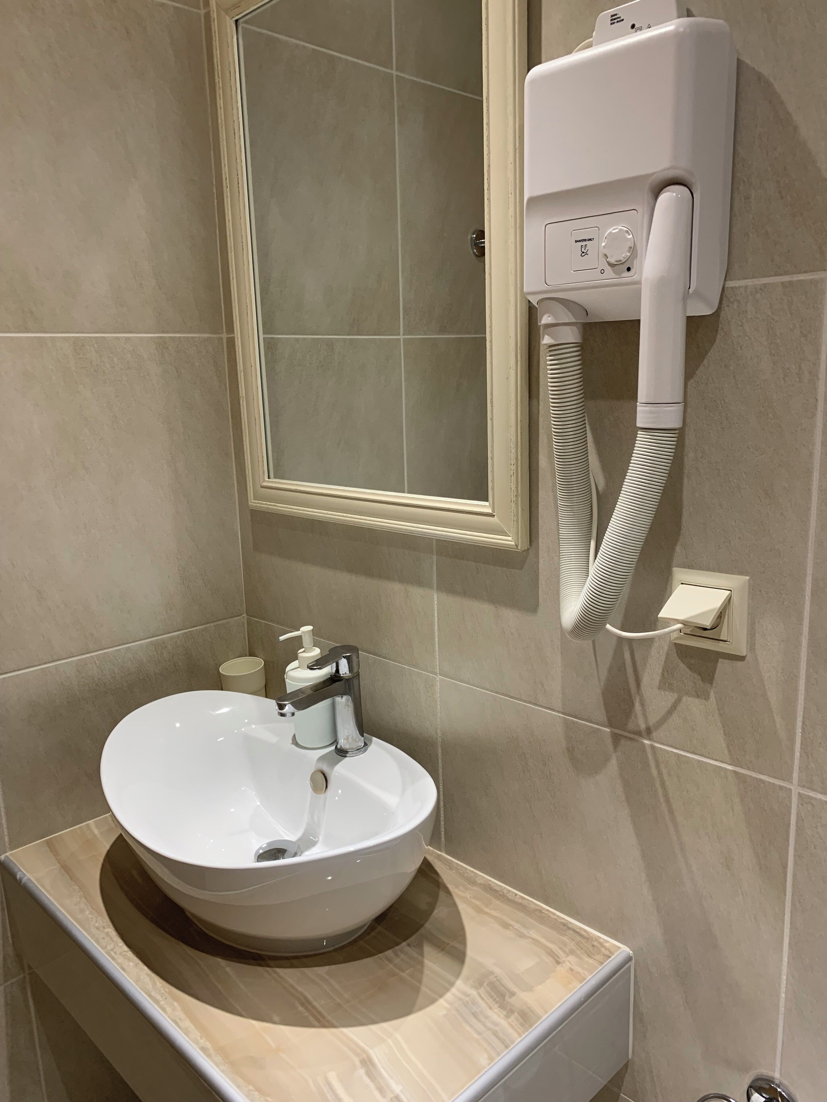 Un baño con un lavamanos blanco, un espejo y un secamanos instalado en la pared.