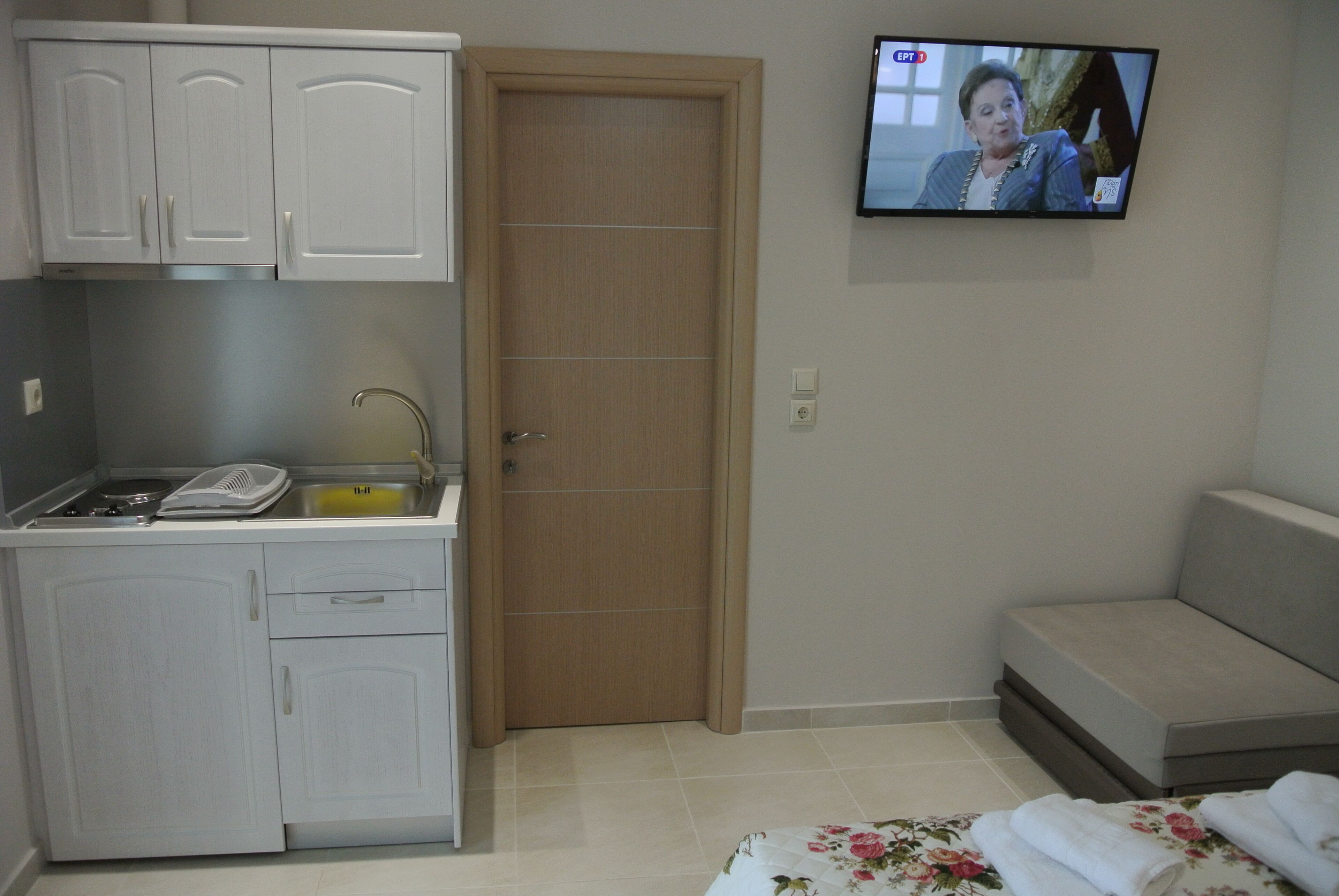 Una habitación pequeña y limpia con kitchenette, una puerta de madera, televisor de pantalla plana y sofá.