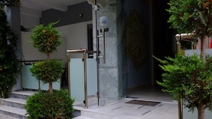 Ingresso di un hotel con porta in vetro, gradini e piante in vaso.
