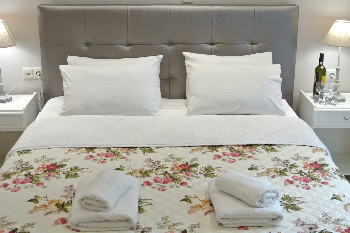 A neatly made bed with a floral quilt, two white pillows, and folded towels on a headboard with a grey upholstered panel.