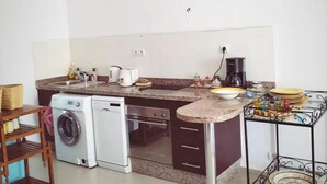A compact kitchen with a washing machine, a coffee maker, and a small dining area. - On the Beach you see Horses and Quad Riders (Essaouira)