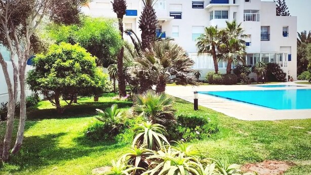 A modern building with a pool, surrounded by lush greenery and palm trees. - On the Beach you see Horses and Quad Riders (Essaouira)