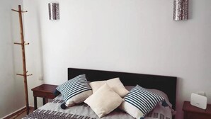 A bedroom with a bed, two bedside tables, a wooden coat rack, and two wall-mounted lamps. - On the Beach you see Horses and Quad Riders (Essaouira)