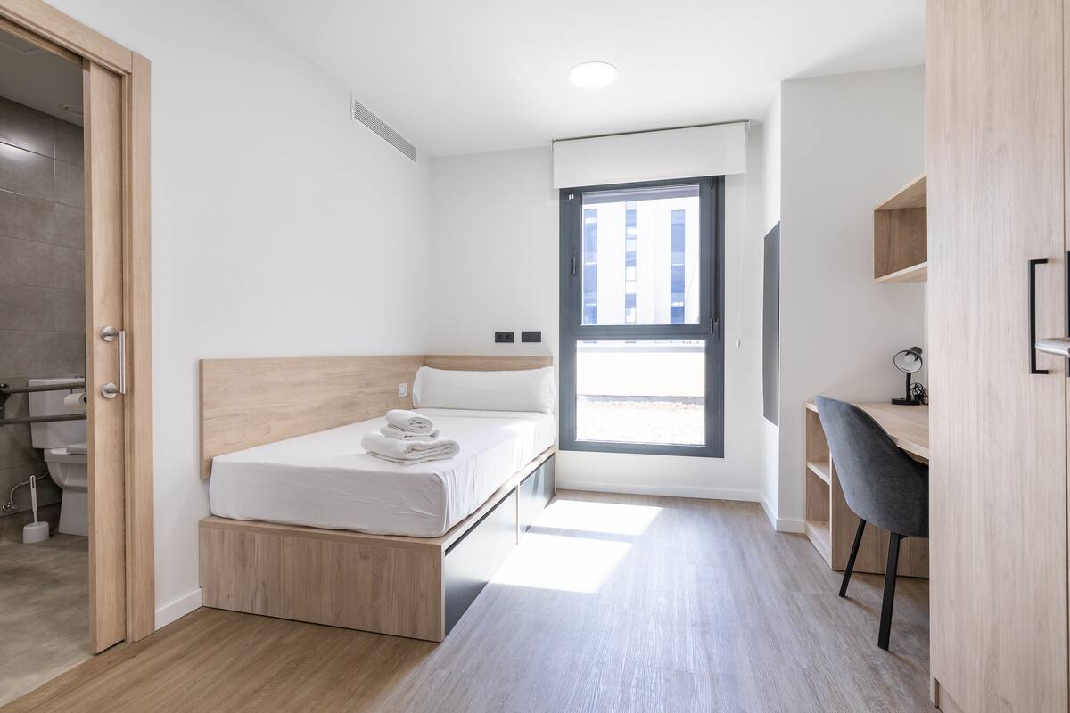 Un dormitorio moderno con una cama, un escritorio y una ventana.