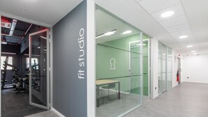 Un espacio de oficina moderno con un panel de vidrio que indica 'fit studio' y un área de gimnasio visible.