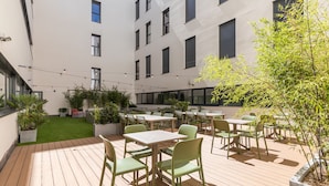 Un patio con mobiliario exterior, césped verde y un edificio con amplias ventanas.