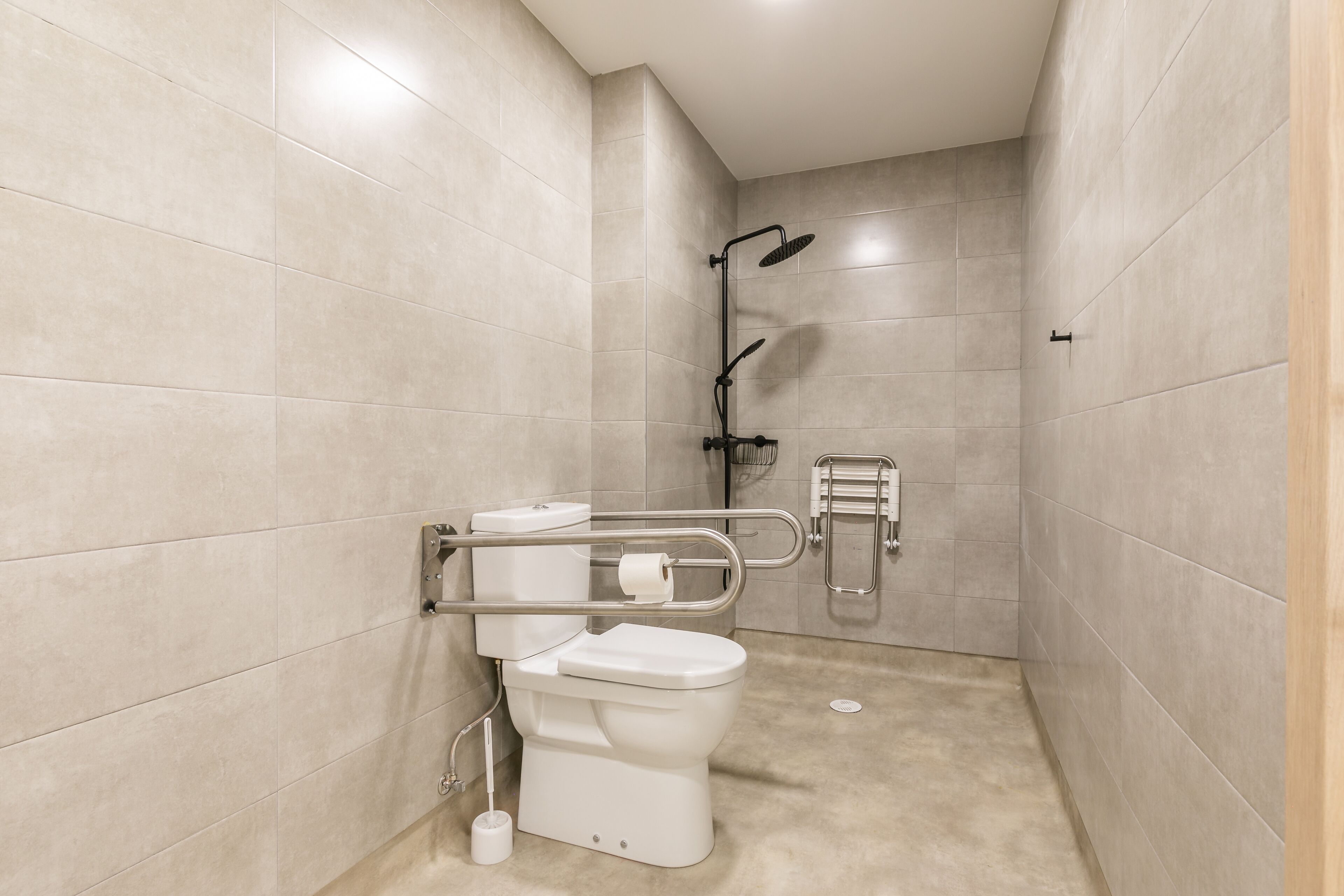 Un baño moderno con inodoro, barras de apoyo, ducha y secador de manos.