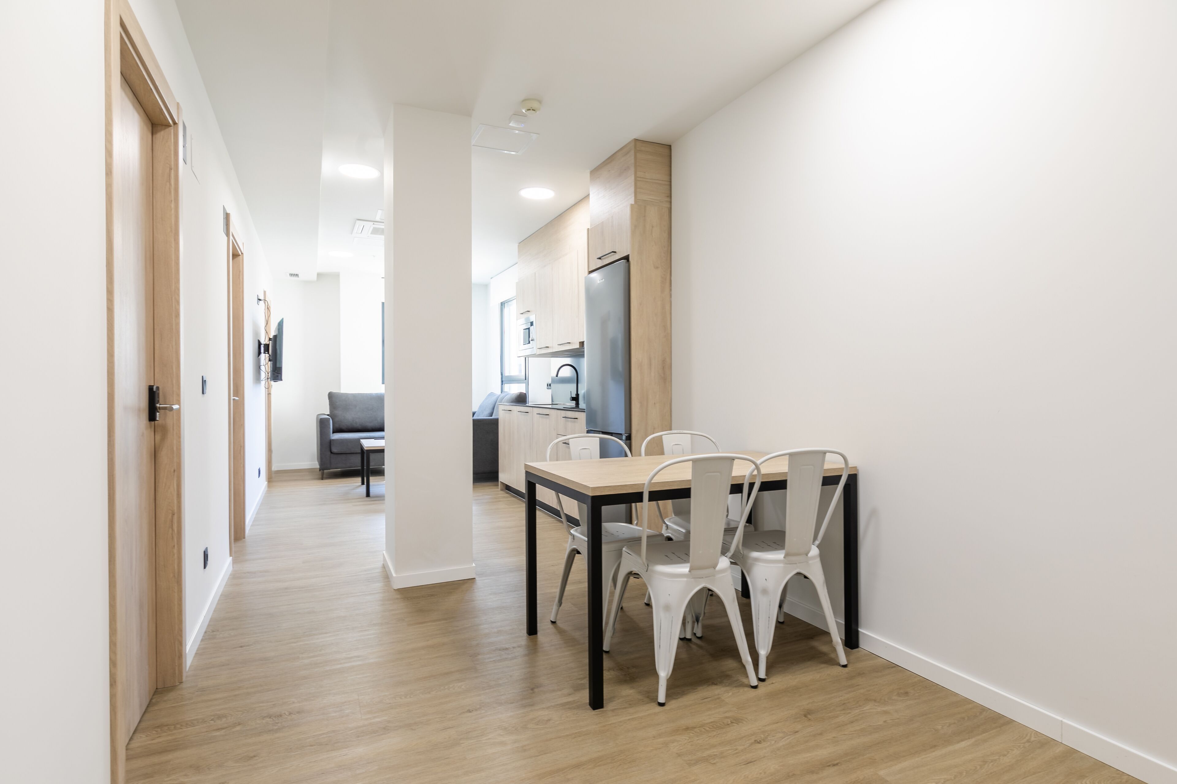 Una cocina moderna con refrigerador, una mesa de comedor con sillas y un sofá gris al fondo.