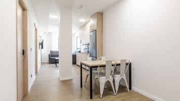 Una cocina moderna con refrigerador, una mesa de comedor con sillas y un sofá gris al fondo.