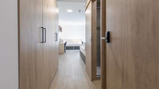 Un pasillo estrecho con puertas de madera que dan a un dormitorio.