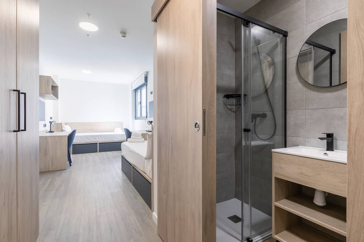 Un baño moderno con cabina de ducha de vidrio, tocador de madera y espejo redondo.