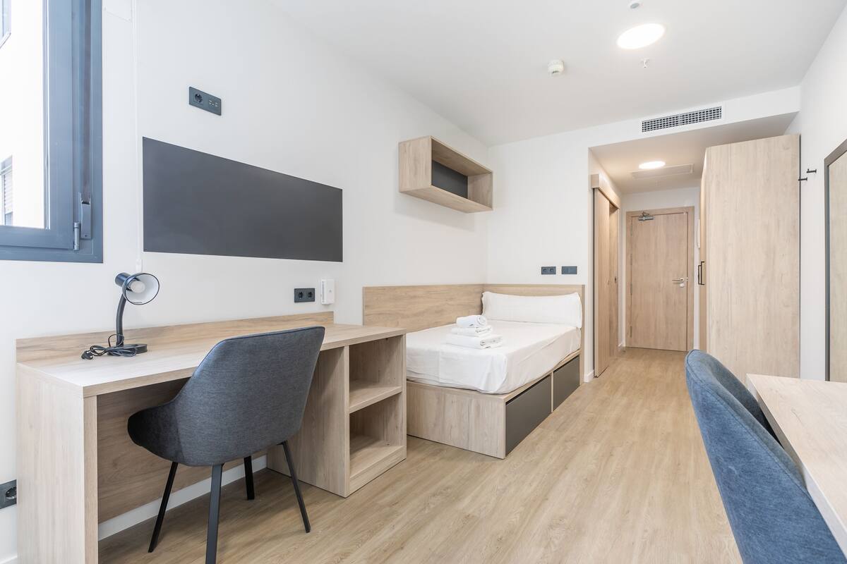 Una habitación pequeña con un escritorio de madera, una silla, una cama y un armario.