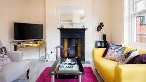 Una sala de estar con televisor, chimenea, un sofá amarillo y una mesa de centro con un libro.