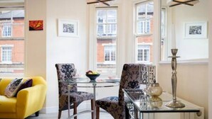 Un salón luminoso con un sofá amarillo, sillones estampados, una mesa de vidrio y un radiador.