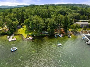 An aerial view of a lakeside property with docked boats, a small dock, and a grassy area with buildings. - Winni Lakefront Cabin (Laconia)