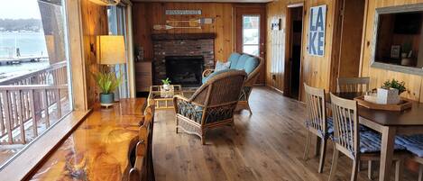 A wooden interior with a dining area, a fireplace, and a view of the water outside.