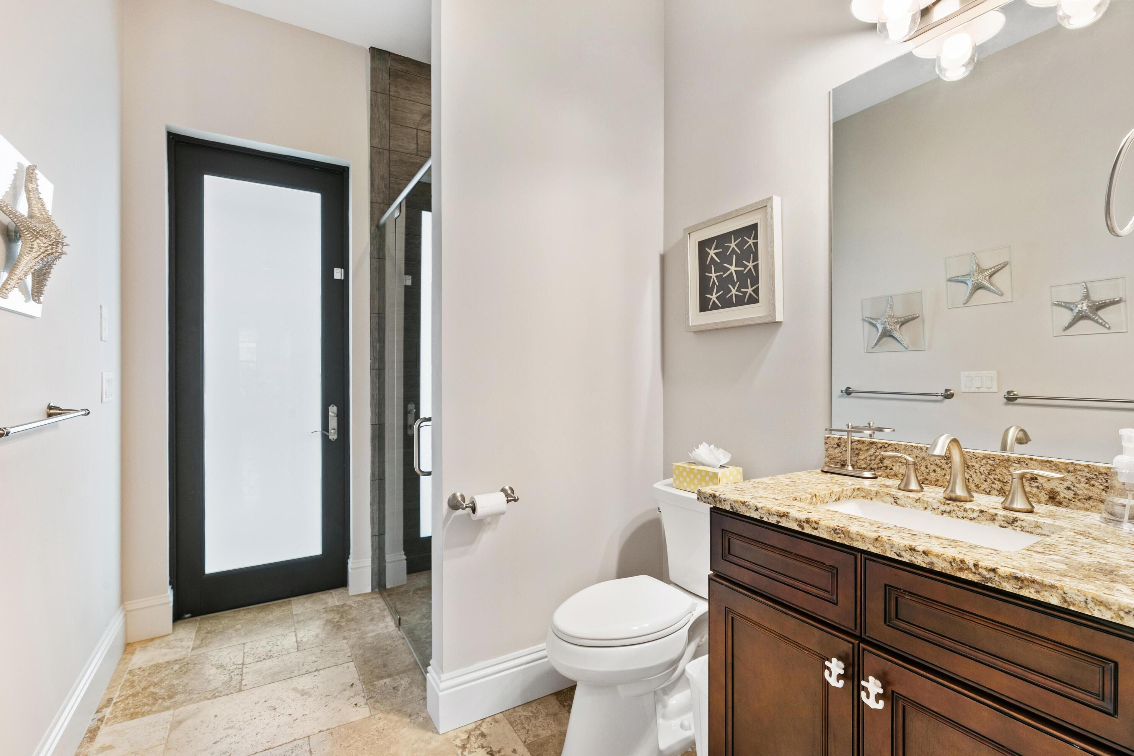 Une salle de bain avec des toilettes blanches, un lavabo doté d’un plan de travail en granit et un miroir au-dessus du lavabo.