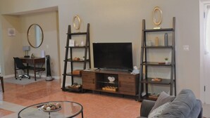 Una sala de estar con televisor, estantes de madera, una mesa de centro de vidrio y un sofá.