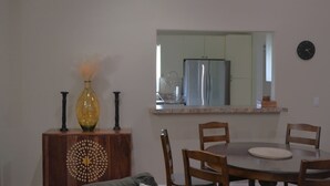 Un comedor con una mesa redonda, cuatro sillas de madera, un florero con plantas secas y un aparador decorativo con un diseño circular.
