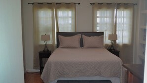 Una cama bien hecha con cubrecama acolchado, dos mesitas de noche con lámparas y un banco al pie de la cama.