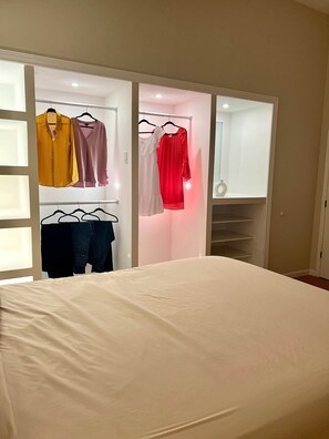 A bedroom with a bed, a closet with hanging clothes, and a door leading to a bathroom.