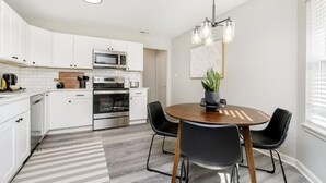 Een moderne keuken met witte kasten, een magnetron, oven en een eethoek met een ronde tafel en stoelen.