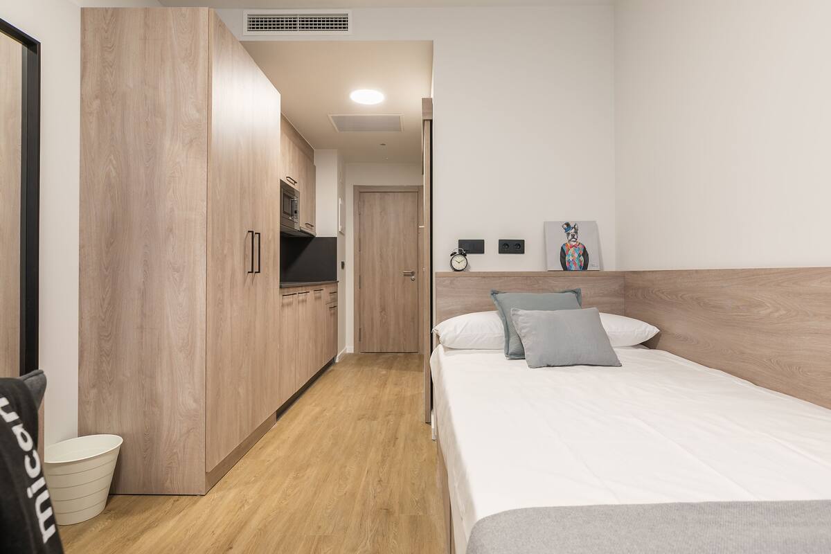 Una habitación de hotel con un armario de madera, una cama con almohadas, una mesita pequeña y un reloj de pared.