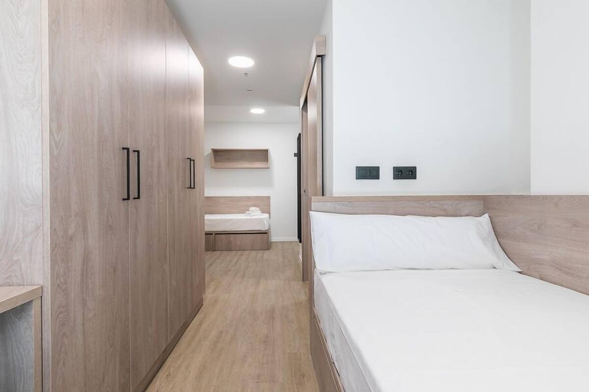 Un dormitorio moderno con un armario de madera, una cama con ropa de cama blanca y una mesita de noche pequeña.