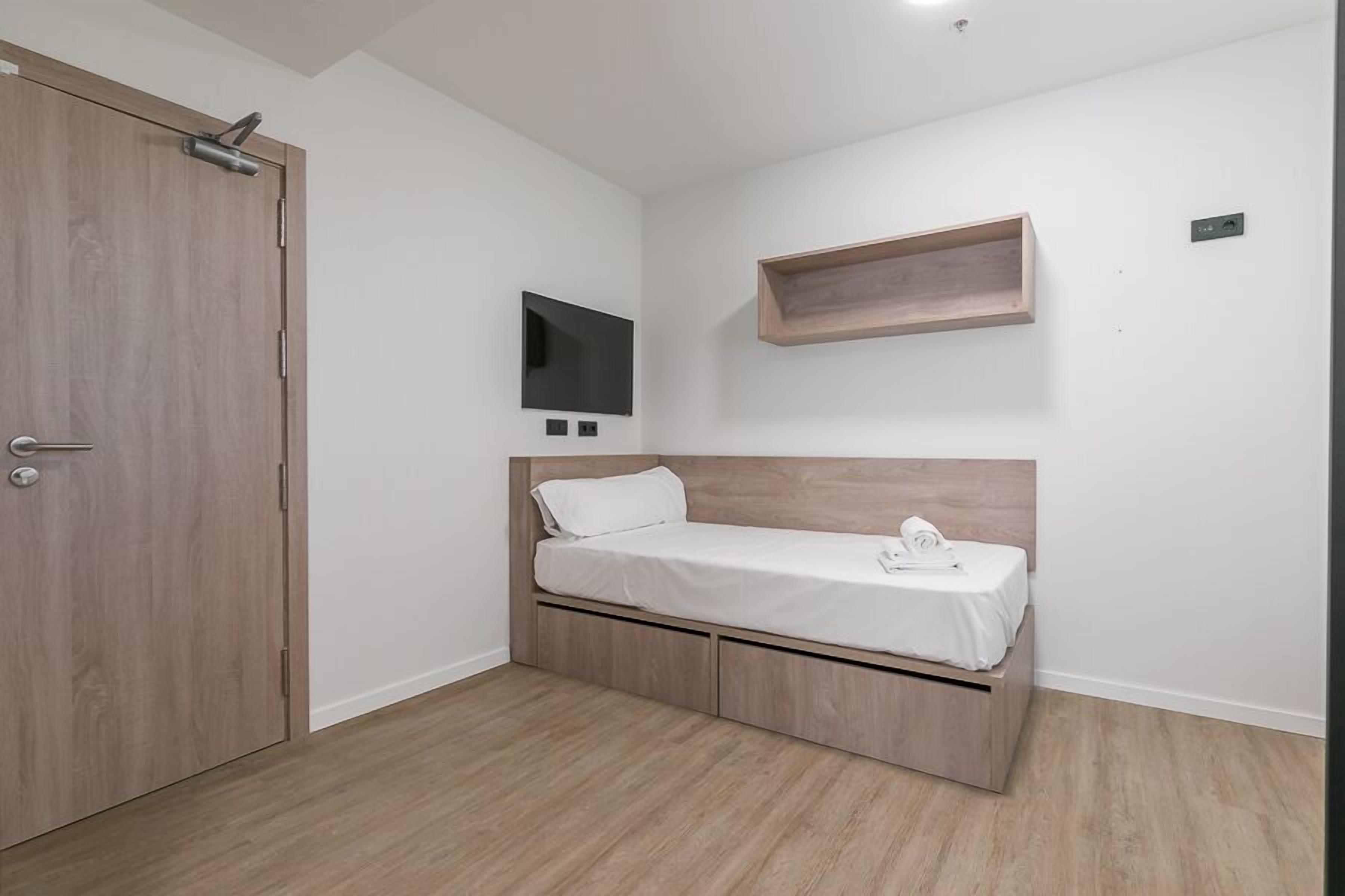 A bedroom with a bed, a TV, and a wooden shelf.