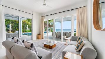 A modern living room with a large glass door leading to a pool area, a ceiling fan, and a view of the ocean.