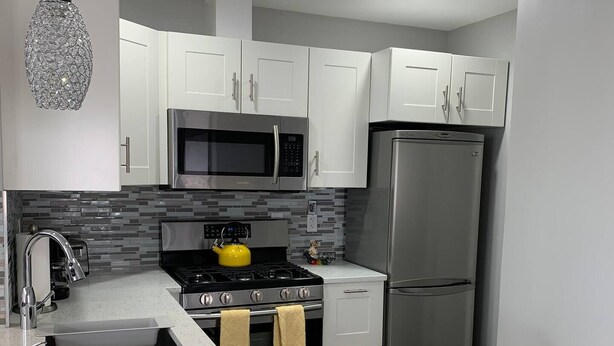 A modern kitchen with white cabinets, stainless steel appliances, a granite countertop, and a unique crystal pendant light. - Your Bright, Confortable, Cozy Second Home

 (Livingston)