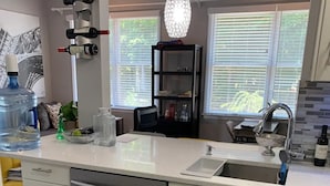 A modern kitchen with a stainless steel dishwasher, white cabinets, a large water dispenser, and a wine rack. - Your Bright, Confortable, Cozy Second Home

 (Livingston)