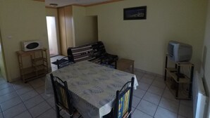 A dining area with a table, chairs, a sofa, a television, and a microwave.