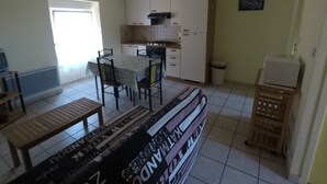 A compact kitchen with white cabinets, a dining table with chairs, a bench, and a small refrigerator.