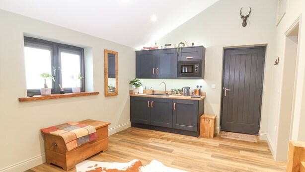 Una cocina moderna con armarios oscuros, un microondas y un lavabo. Hay un banco de madera y una alfombra de cuero de vaca en el suelo.