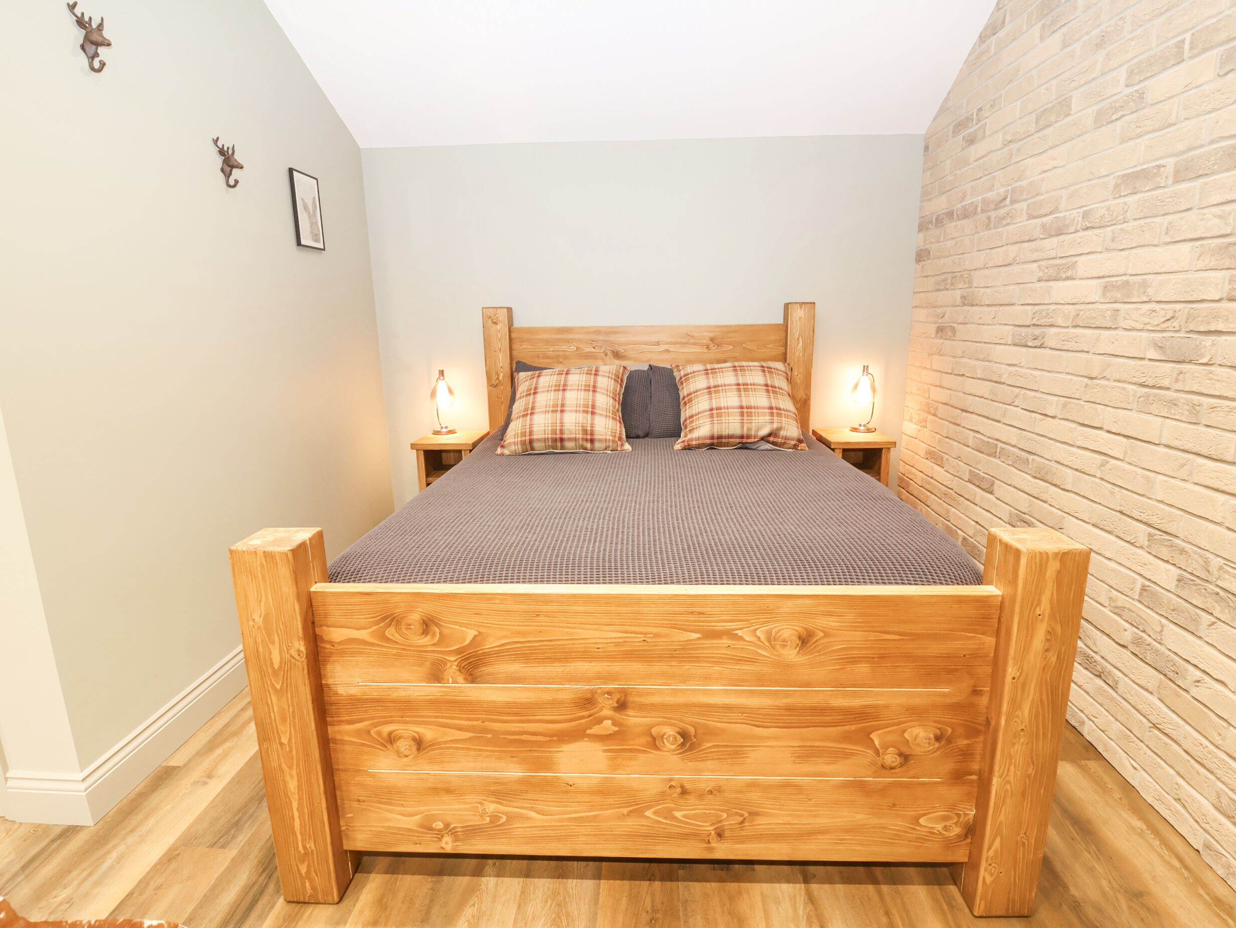 Una cama de madera con cabecera, dos mesitas de noche con lámparas y una pared de ladrillo.
