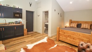 Un dormitorio con cama de madera, alfombra de cuero de vaca y una cocina con armarios oscuros y un microondas.