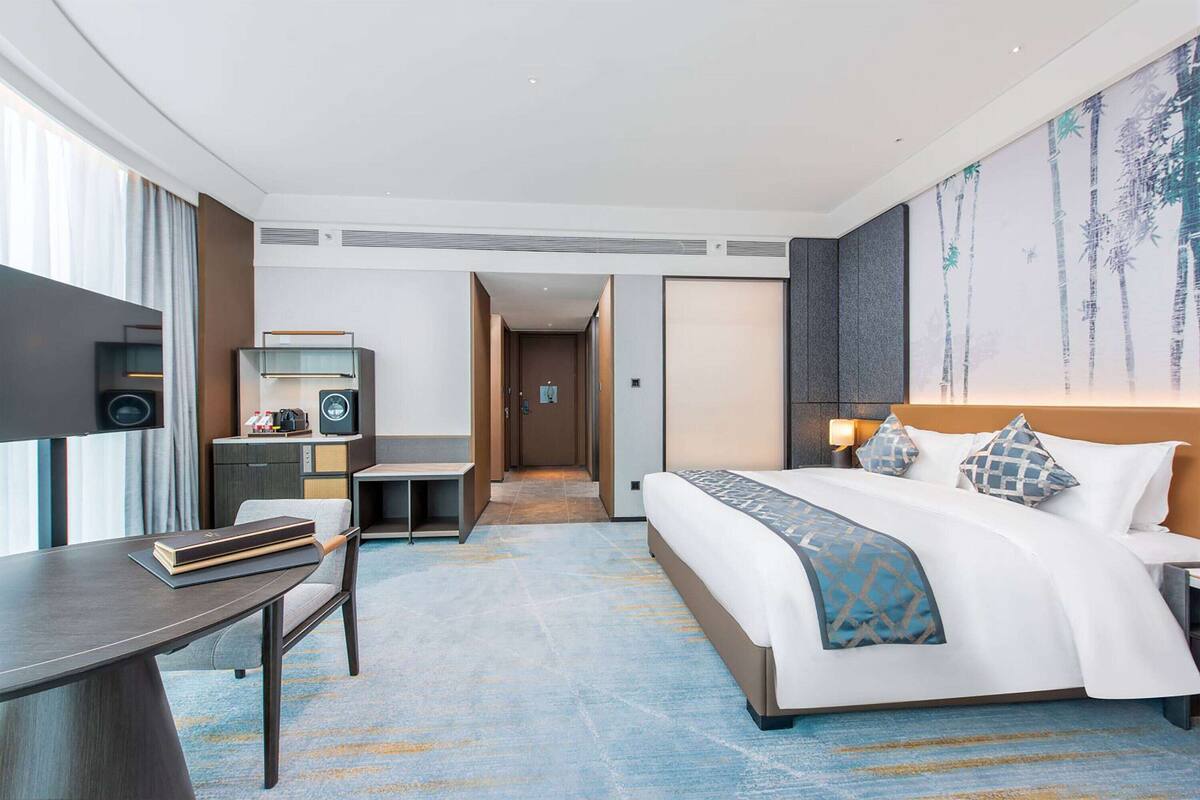Ein Hotelzimmer mit Bett, Schreibtisch, Stuhl und einem großen Gemälde an der Wand.