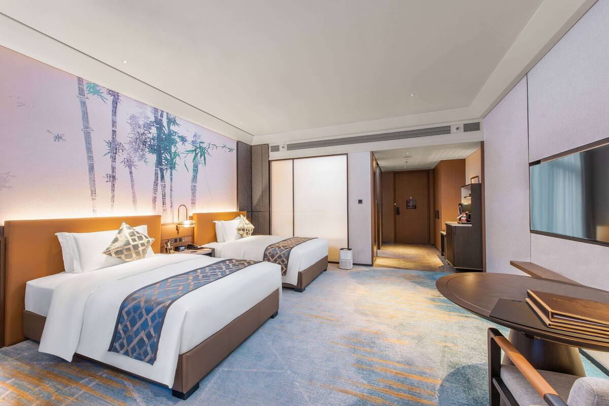 Ein Hotelzimmer mit zwei Betten, einem Schreibtisch, einem Stuhl, einem Fernseher und einem durch eine geöffnete Tür einsehbaren Badezimmer.